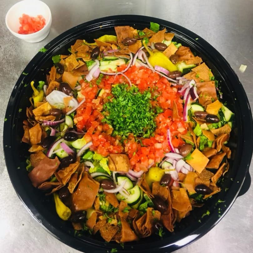 Large Mediterranean fattoush salad with lettuce, tomatoes, cucumbers, onions, olives, and pita chips.