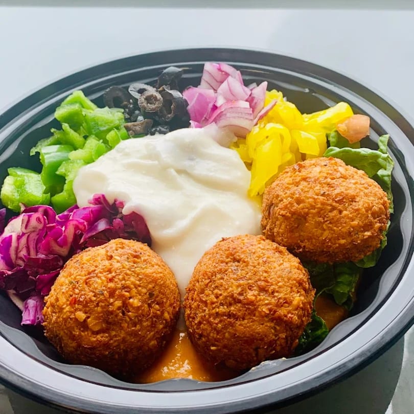 A Pita Express falafel bowl with green peppers, red cabbage, olives, pickled onions, and white sauce.