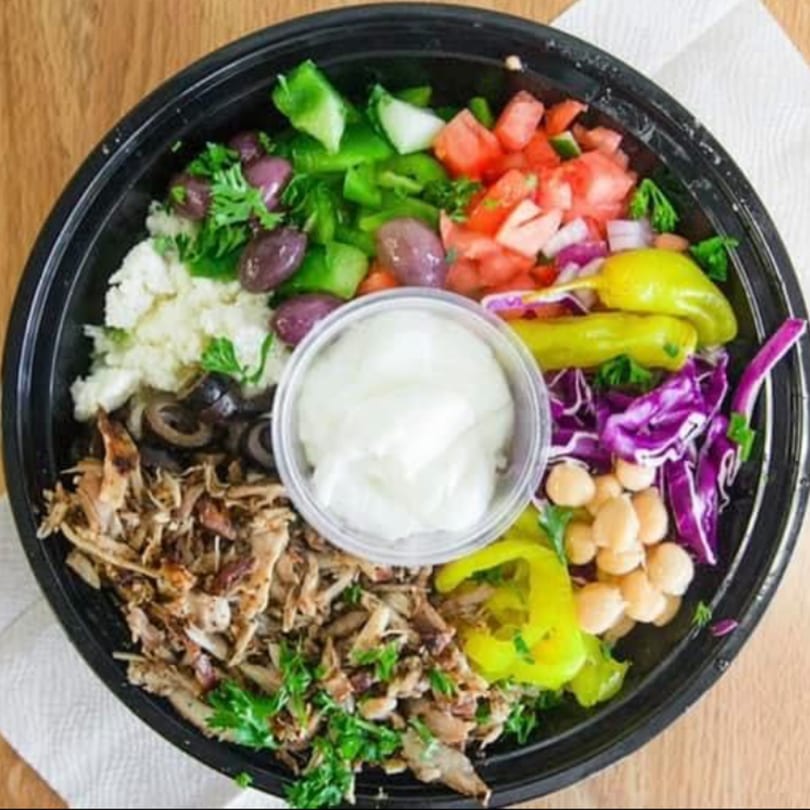 Overhead view of a Mediterranean bowl with chicken, olives, feta, tomatoes, peppers, chickpeas, and sauce.