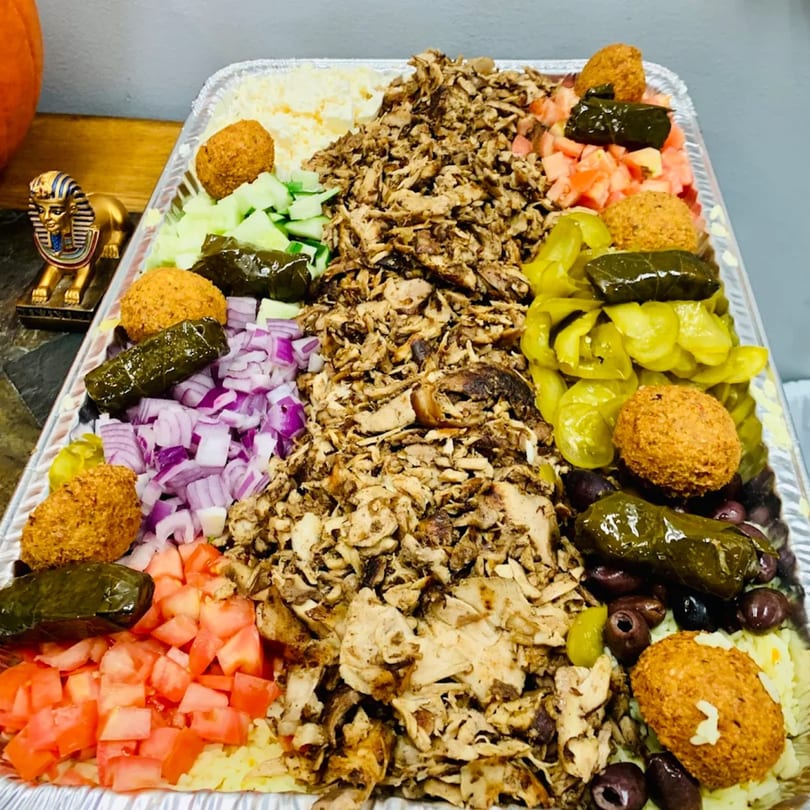 A large catering tray from Pita Express filled with Mediterranean food, including shawarma, falafel, and various vegetables.