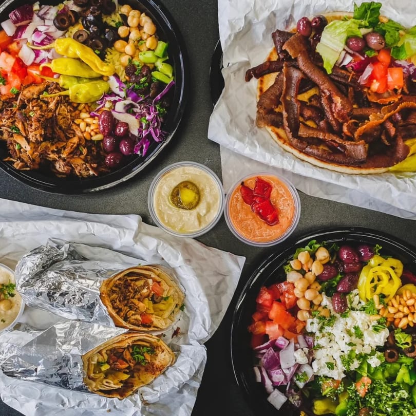 Overhead view of Pita Express Mediterranean dishes: two bowls, a gyro, two wraps, and two dips.